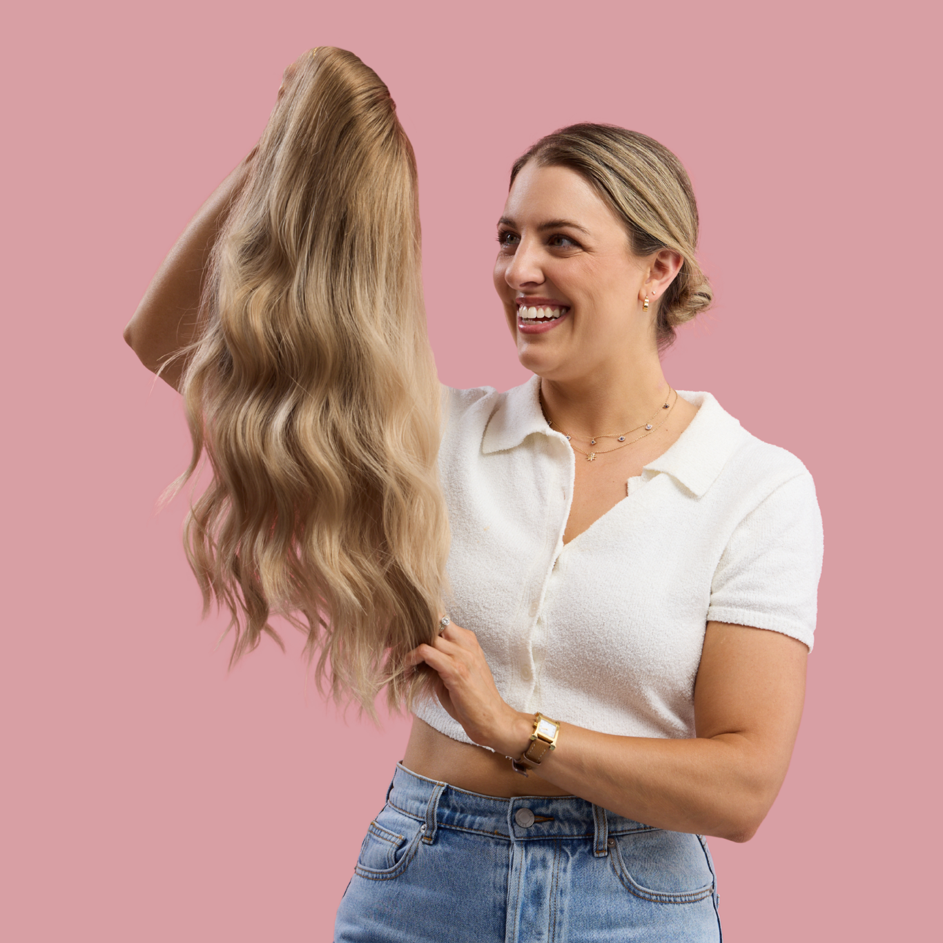Woman holding a long blonde wig against a pink background